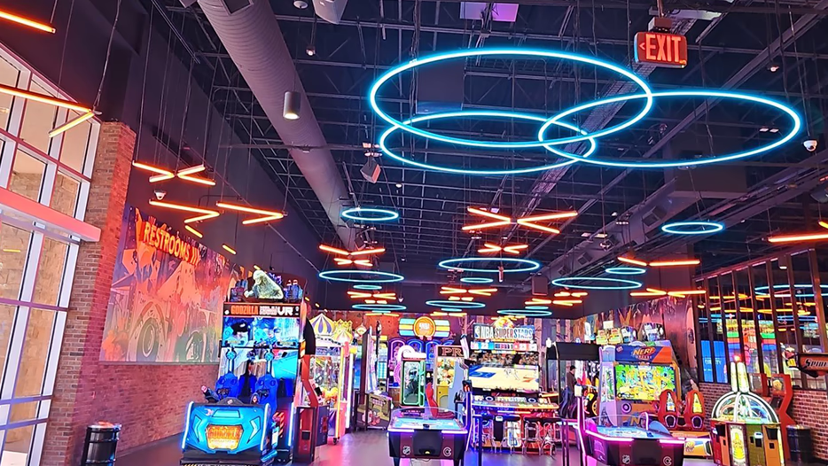 Commercial arcade lighting by Modern Electric 
with suspended blue neon rings and orange accent lights above the games