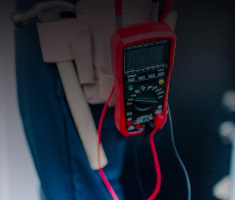 Electrician's red digital multimeter and hand tools clipped to a tool belt on a Modern Electric job