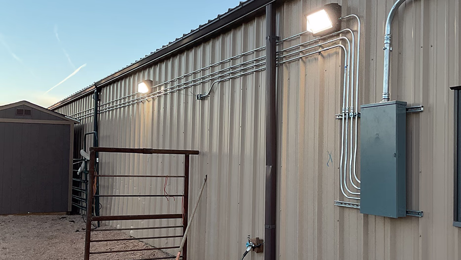 Modern Electric exterior electrical panel and 
conduit runs feeding wall-pack flood lights on a metal farm building