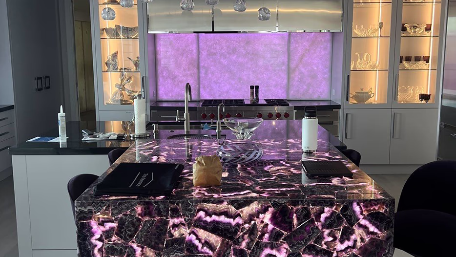 Luxury kitchen wired by Modern Electric with a 
backlit purple onyx island, backsplash, and lit glass display cabinets
