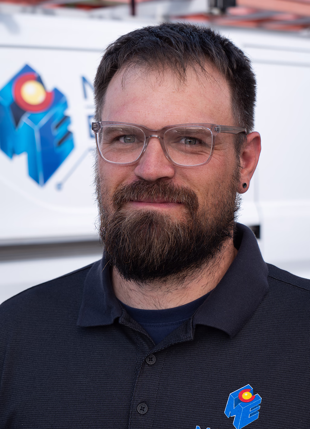 Sean, Lead Residential Electrician at Modern Electric, wearing glasses in front of a company service van
